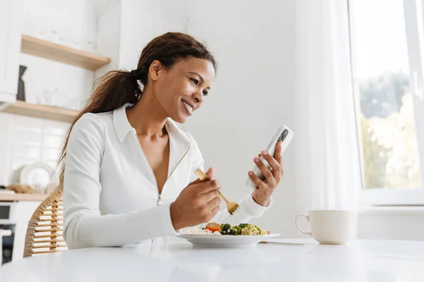 Young Black Woman Using Cellphone While Having Lunch Kitchen Home — Stock Fotó