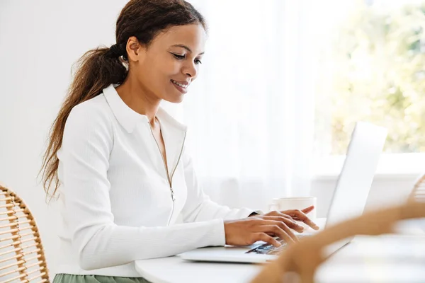 Black woman smiling while working with laptop in kitchen at home