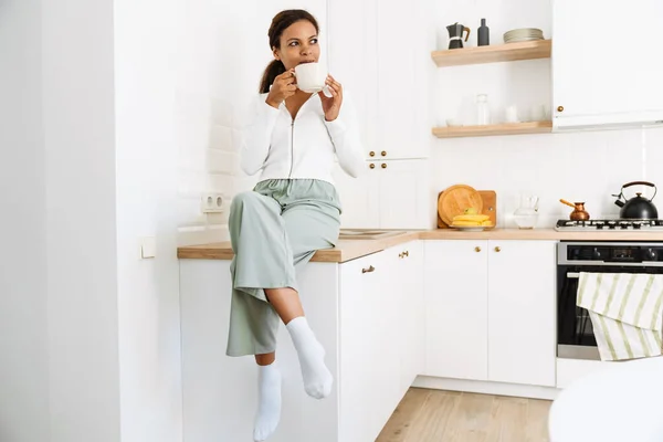 Black woman smiling while drinking tea in kitchen at home