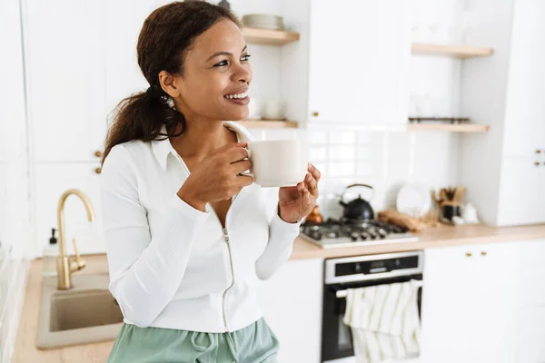 年轻的黑人女人在家里厨房喝咖啡的时候笑了 — 图库照片