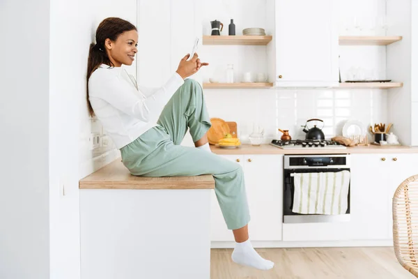 Young Black Woman Smiling While Using Cellphone Kitchen Home — Stock Fotó