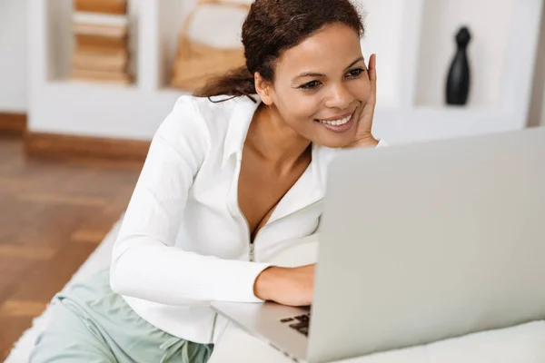 年轻的黑人妇女坐在家里的地板上用笔记本电脑工作 — 图库照片