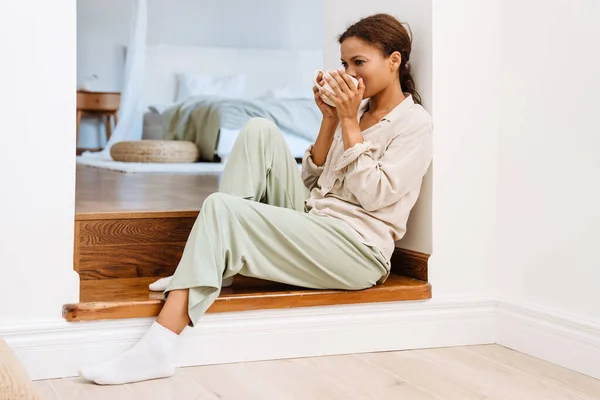 坐在楼梯上喝茶的黑人妇女穿着睡衣 — 图库照片