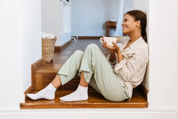 家の階段に座っている間 紅茶を飲みながら笑顔の黒人女性 — ストック写真