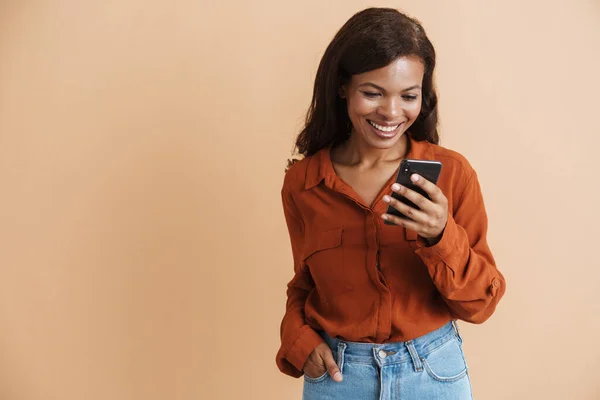 年轻的黑人妇女 身穿衬衫 面带微笑 用手机与米色背景隔离 — 图库照片