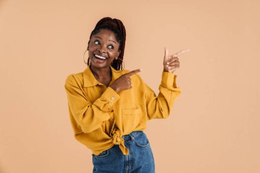 Young black woman with afro pigtails smiling and pointing fingers aide isolated over beige background