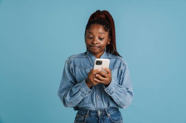 Mavi arka planda izole edilmiş cep telefonu kullanan siyah saçlı genç bir kadın.