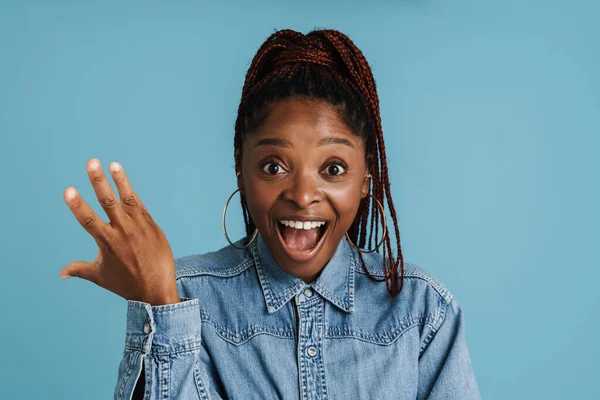 Siyah saçlı genç bir kadın mavi arka planda izole edilmiş kameraya şaşırdığını ifade ediyor.