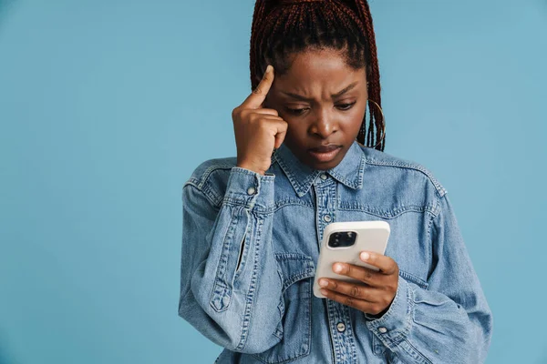 青の背景に隔離された携帯電話を使用してアフロピグテールを持つ若い黒人女性 — ストック写真