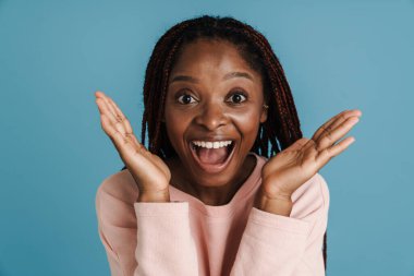 Siyah saçlı genç bir kadın mavi arka planda izole edilmiş kameraya şaşırdığını ifade ediyor.