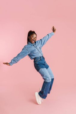 Genç siyahi kadın pembe arka planda izole bir şekilde kameraya dans ediyor.