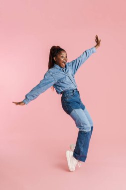Genç siyahi kadın pembe arka planda izole bir şekilde kameraya dans ediyor.