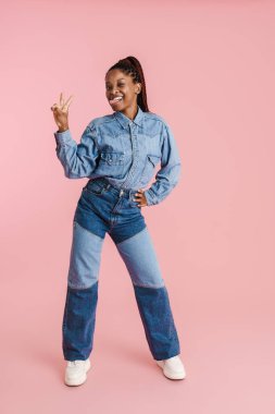 Dilini gösteren ve pembe arka planda izole bir şekilde kameraya göz kırpan genç siyahi kadın.