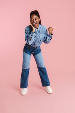 Genç siyah kadın gülüyor ve pembe arka planda izole edilmiş bir şekilde işaret ediyor.