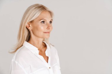 Tişört giyen olgun sarışın kadın beyaz arka planda yalnız başına poz veriyor ve yan tarafa bakıyor.