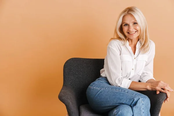 Mature Blonde Woman Smiling Camera While Sitting Chair Isolated Beige — 스톡 사진