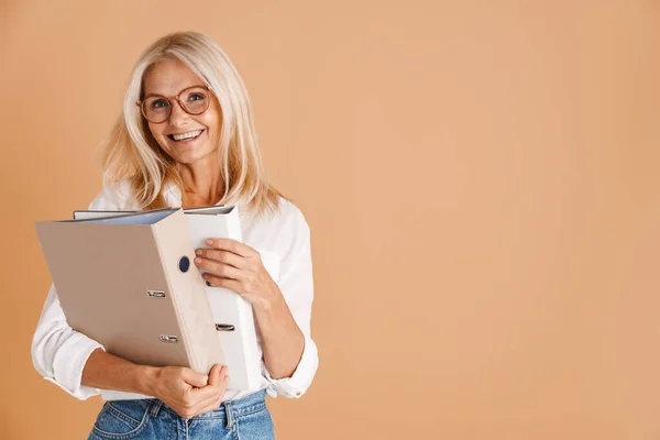 Mature Woman Eyeglasses Smiling Holding Paper Folders Isolated Beige Background — Zdjęcie stockowe
