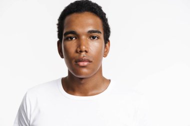 Genç siyah adam tişört giyip beyaz duvarın üzerinden izole edilmiş kameraya bakıyor.