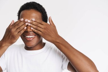 Young black man in t-shirt smiling while covering his eyes isolated over white background
