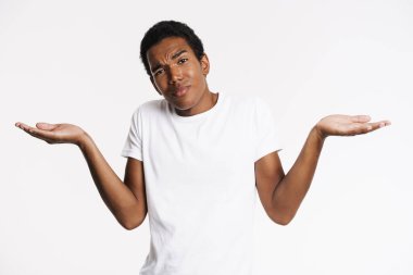 Genç siyahi adam beyaz duvarın üzerinde izole edilmiş telif alanını tutarken kaşlarını çatıyor