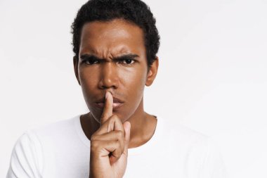 Genç siyah adam beyaz duvarın üzerinde izole edilmiş kameraya sessiz bir jest yapıyor.