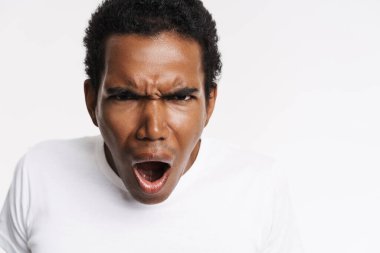 Beyaz arka planda izole edilmiş kameraya bağırırken kaşlarını çatan genç siyahi bir adam.