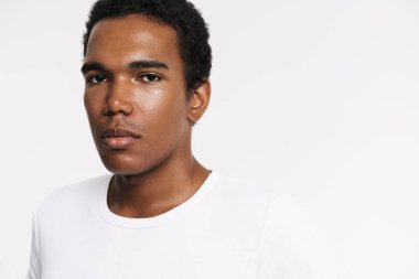 Genç siyah adam tişört giyip beyaz duvarın üzerinden izole edilmiş kameraya bakıyor.