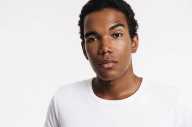 Young black man dressed t-shirt posing and looking at camera isolated over white wall