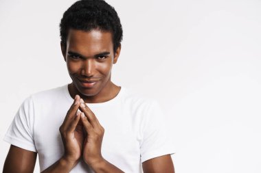 Genç siyahi adam tişört giymiş gülümsüyor ve ellerini yan yana tutuyor.