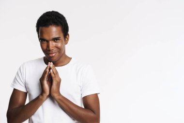 Genç siyahi adam tişört giymiş gülümsüyor ve ellerini yan yana tutuyor.