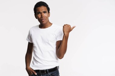 Genç siyahi adam tişörtünü giyip parmak kaldırıyor ve beyaz duvar yüzünden kaşlarını çatıyor.