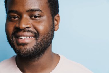 Siyah kıllı adam mavi arkaplanda izole edilmiş kameraya bakarken gülümsüyor.