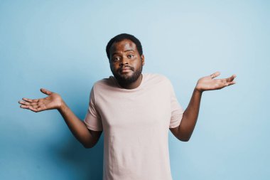 Kopyalama alanını mavi arkaplan üzerinde izole ederken siyah kafası karışmış bir adam kameraya bakıyor