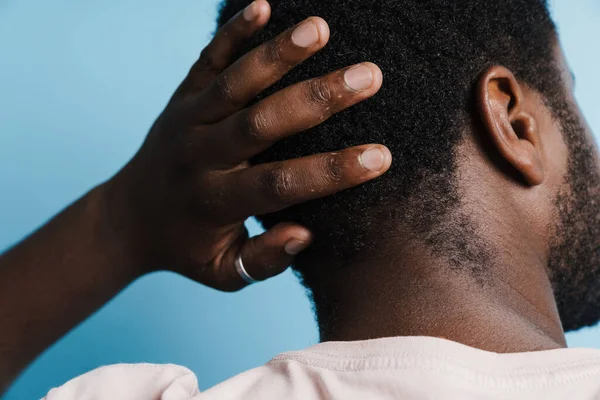 Tişörtlü siyah tüylü adam kafasının arkasını ovalıyor. Mavi arka planda izole edilmiş.