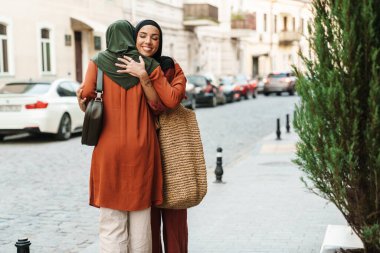 Şehir caddesindeki toplantı sırasında gülümseyen ve sarılan çok ırklı Müslüman kadınlar.