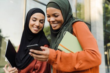 Şehir caddesinde yürürken cep telefonu kullanan çok ırklı Müslüman kadınlar