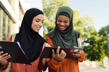 Multiracial muslim women examining documents together while standing on city street