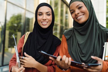 Çok ırklı Müslüman kadınlar dışarıda panolarla dururken gülümsüyorlar.