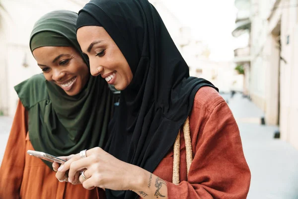 Multiraciální Muslimské Ženy Pomocí Mobilního Telefonu Při Chůzi Ulici — Stock fotografie