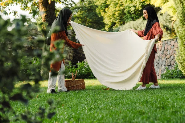 Çok ırklı Müslüman kadınlar yeşil parkta piknik için yer açıyor.