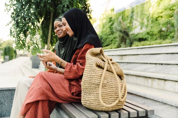 多种族穆斯林妇女坐在室外长椅上使用手机 — 图库照片