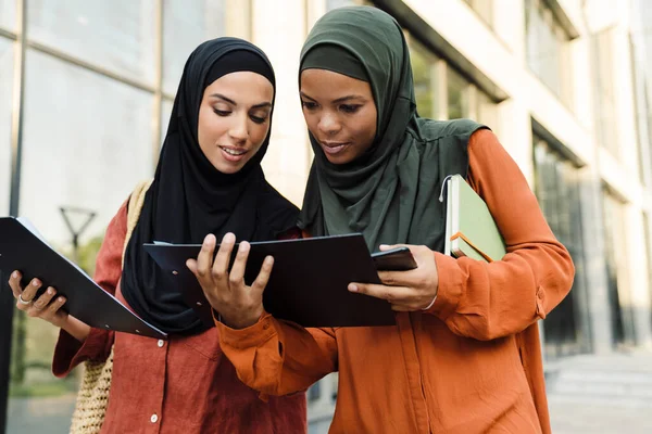 Çok ırklı Müslüman kadınlar, şehir sokaklarında dururken birlikte belgeleri inceliyorlar.
