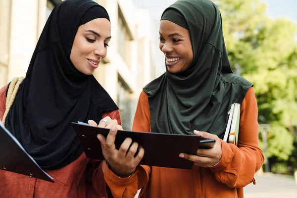 Çok ırklı Müslüman kadınlar, şehir sokaklarında dururken birlikte belgeleri inceliyorlar.
