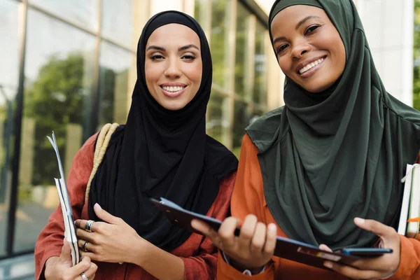 Çok ırklı Müslüman kadınlar dışarıda panolarla dururken gülümsüyorlar.