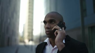 Ciddi bir Afrikalı işadamı sokakta telefonla konuşuyor.
