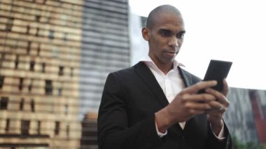 Handsome African businessman typing by mobile on the street
