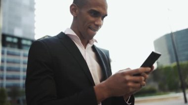 Gülümseyen Afrikalı işadamı sokakta cep telefonuyla yazıyor.
