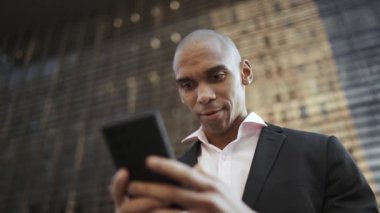 Güzel Afrikalı işadamı sokakta cep telefonuyla mesajlaşıyor.