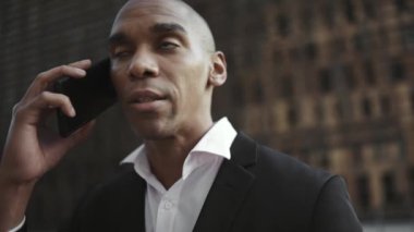 Yoğunlaşmış Afrikalı işadamı sokakta telefonla konuşuyor.