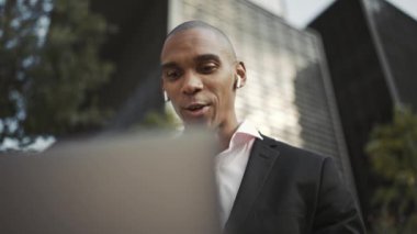 Diz üstü bilgisayarda çalışan ve kulaklıkla konuşan neşeli Afrikalı işadamı.